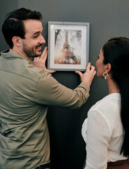 Man, woman and hanging picture frame on office wall with decision, test and interior design at startup. Business people, partnership and art for decoration, style and teamwork at architecture agency