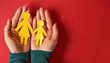 © Carlostock - Hands holding a family recreated in yellow paper, consisting of a mother and daughter, on a red background. The person holding the concept of family unity is wearing a green sweater