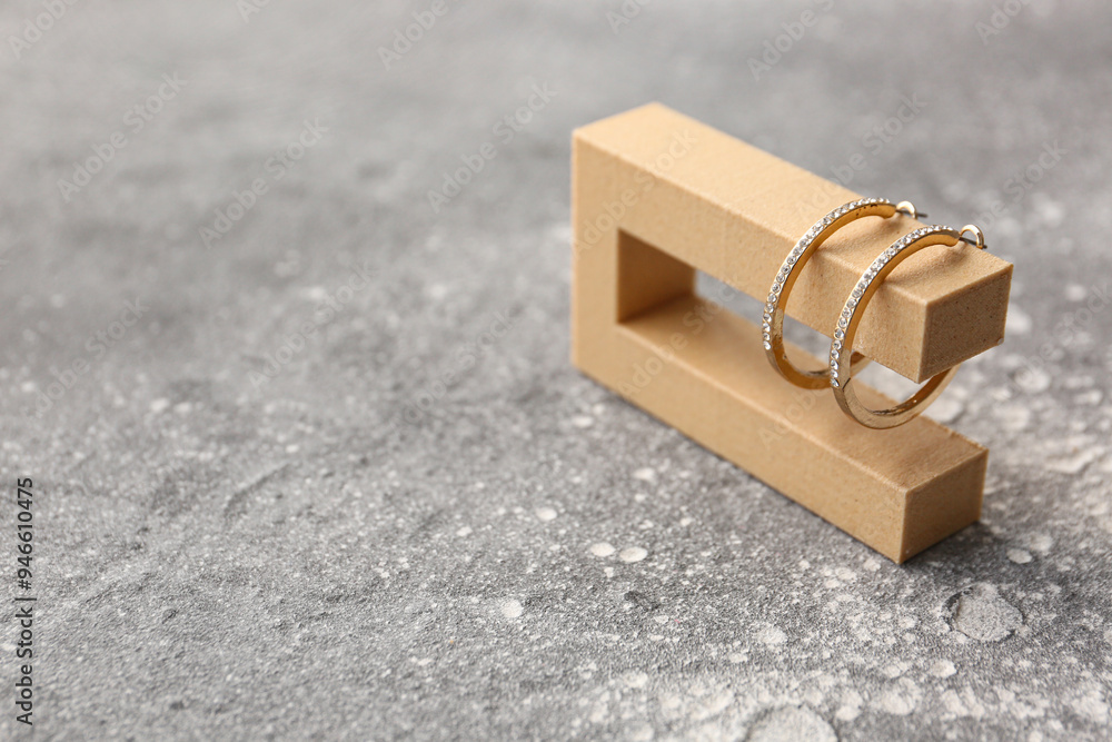Decorative podium with beautiful golden earrings on grunge grey background
