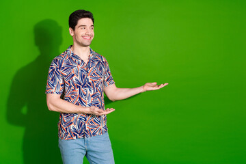 Photo of nice guy with stylish haircut dressed print shirt hands demonstrate product look empty space isolated on green color background