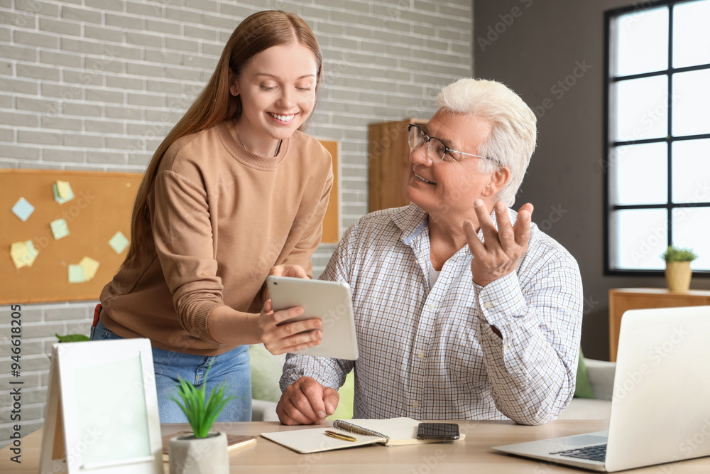 Senior man with his granddaughter using tablet computer at home