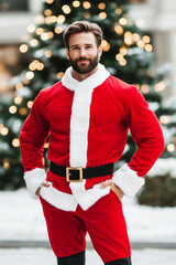 Wall Mural - Traditional Christmas outfit with a man in a red Santa suit complete with black boots and belt festive scene with snow and holiday lights surrounding him 