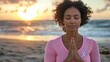 © keetazalay - A serene image of a breast cancer survivor meditating on a beach at sunrise wearing a pink ribbon t-shirt with her eyes closed and hands in a prayer position symbolizing peace healing and spiritual