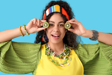 Canvas Print - Beautiful young happy African-American woman with slices of kiwi on blue background