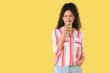 Canvas Print - Beautiful young happy African-American woman with glass of tasty kiwi smoothie on yellow background