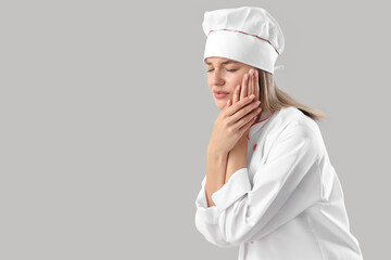 Young female chef suffering from tooth ache on grey background