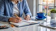 © FatePSE - Woman writing in notebook at desk with cup of coffee