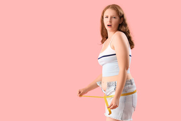 Canvas Print - Upset young woman in tight shorts measuring her hips on pink background. Weight gain concept