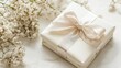 © Olga - A white box gift with bow and flowers on white table against white backdrop