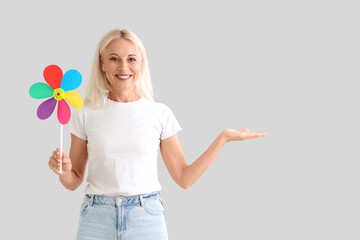 Wall Mural - Mature woman with toy windmill showing something on light background