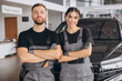 © anatoliycherkas - Auto car repair service center. Two happy mechanics - man and woman standing by the car