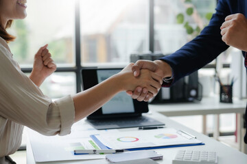 Business partners shaking hands closing a deal after checking financial charts and achieving their business goals