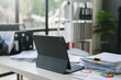 © amnaj - Modern office desk with a tablet computer showing financial reports and paperwork, suggesting a busy work environment