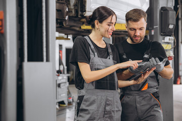 Young expert female inspects repair checklist with automotive mechanic worker partner, quality suspension technician team at fix garage. Vehicle maintenance service works industry occupation job.