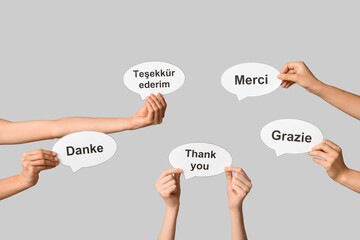 Female hands holding speech bubbles with text THANK YOU in different languages on grey background