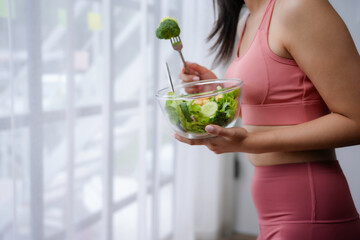 Woman in sportswear happily eats a fresh salad at home after working out, focusing on a healthy lifestyle with plant based meals