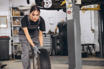 Wall Mural - Smiling Charming Woman Car mechanic holding tire at repair garage. Replacement of winter and summer tires.