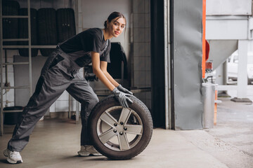 Wall Mural - Smiling Charming Woman Car mechanic holding tire at repair garage. Replacement of winter and summer tires.