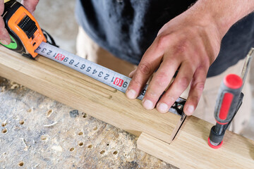 The carpenter measures the cut on the oak part with a tape measure