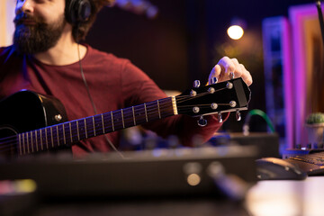 Wall Mural - Sound engineer artist tuning his acoustic guitar strings to play and record new tracks, working with electronic mixing and mastering gear in home studio. Young musician creating cool tunes.