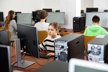 Portrait of interested tween girl during lesson in computer room of school library ..