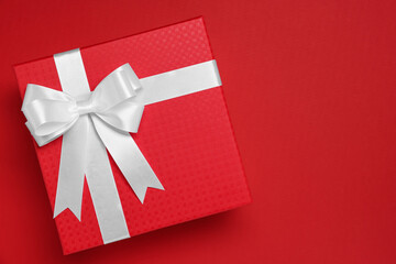 Poster - Gift box with white bow on red background, top view. Space for text