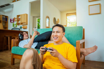 the indonesian man playing a video game and the woman watching a movie on her mobile phone in the li