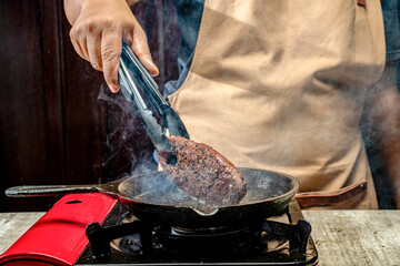 A person is cooking a sirloin steak in a pan on a stove