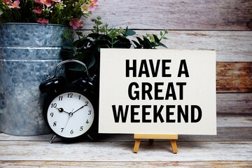 have a great weekend text on paper card and easel standing with alarm clock on wooden background