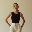 © Leli - A woman showcases her poise and fashion sense dressed in a sleek black top and tailored white trousers Her serene expression and posture reflect sophistication in a simple elegant setting