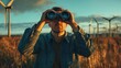 © AGCreative - A man observes nature using binoculars amidst a field of wind turbines, enjoying the scenic landscape at dusk.