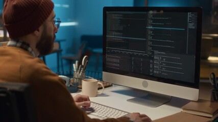 Medium back view of unrecognizable young male programmer living with disability sitting at desk in IT office maintaining computer systems and servers