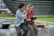 © Kittipong - Two Asian students are sitting and talking about work in front of a modern building.