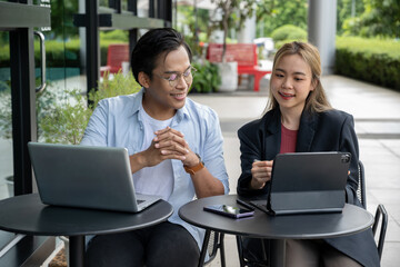 Two businessmen discussing work using tablets and laptops in a modern coffee shop.