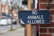 © watz - A weathered wooden sign with white paint, reading No Animals Allowed, is attached to a post outside a brick building..
