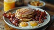 © MINMIN - A plate of pancakes, bacon, fried eggs, and a glass of orange juice. A classic breakfast meal.