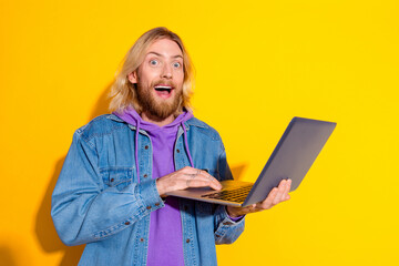 photo portrait of handsome young guy hold netbook amazed wear trendy jeans outfit isolated on yellow