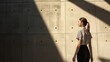 © fotofabrika - A woman walks along a textured concrete wall, bathed in natural light and shadow in a modern architectural space during the afternoon