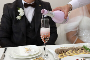 Wall Mural - The glasses of the bride and groom are filled with sparkling wine at the festive table.