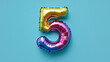 © KotBaton - Rainbow foil balloon number five. Top view. Colored number on blue background.