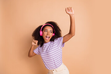 Poster - Portrait of pretty young girl dancing headphones wear striped t-shirt isolated on beige color background