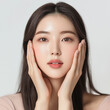 © vilaiporn - Korean woman with long hair and hands on her face wearing a light pink top on a white background. Makeup for skincare product advertisement in clean and simple style.