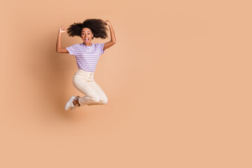 Wall Mural - Full size photo of pretty young woman jump raise fists wear t-shirt isolated on beige color background