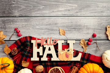 Wall Mural - Autumn flat lay composition. Red plaid with pumpkins, red berries, dry leaves, nuts, Hello Fall sign on wooden desk table. Flat lay, top view.