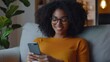 © Ace64 Studio - Cropped shot of an african-american young woman using smart phone at home. smiling african american woman using smartphone at home messaging or browsing social networks while relaxing on couch.