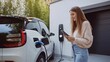© milkyway - Young woman with smartphone waiting while her electric car charging at home charging
