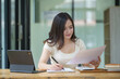 © Songsak C - Asian businesswoman working on a digital tablet and reading documents on desk in office.