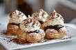 © Zivorad - Four delectable cream-filled pastries topped with rich chocolate and whipped cream, perfectly presented on a white plate with chocolate shavings surrounding them.