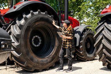 A woman with a digital tablet in her hand touches a large wheel of a construction or agricultural machine. Ag equipment dealership.