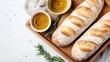 © JoxyAimages - Rustic baguettes with diagonal slashes, accompanied by a small bowl of olive oil and decorated with rosemary sprigs, displayed on a wooden board against a white backdrop.